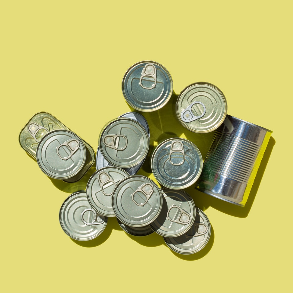Assortment of different canned preserved vegetables, meat, fish, seafood in tin cans. Tinned fish rich in omega 3 fatty acids. Flat lay top view yellow background