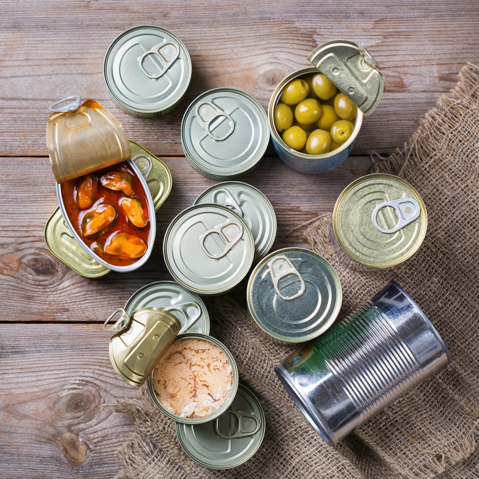 Assortment of different canned preserved vegetables, meat, fish, seafood in tin cans on a wooden table. Non-Perishable goods, food, donations concept. Flat lay top view background