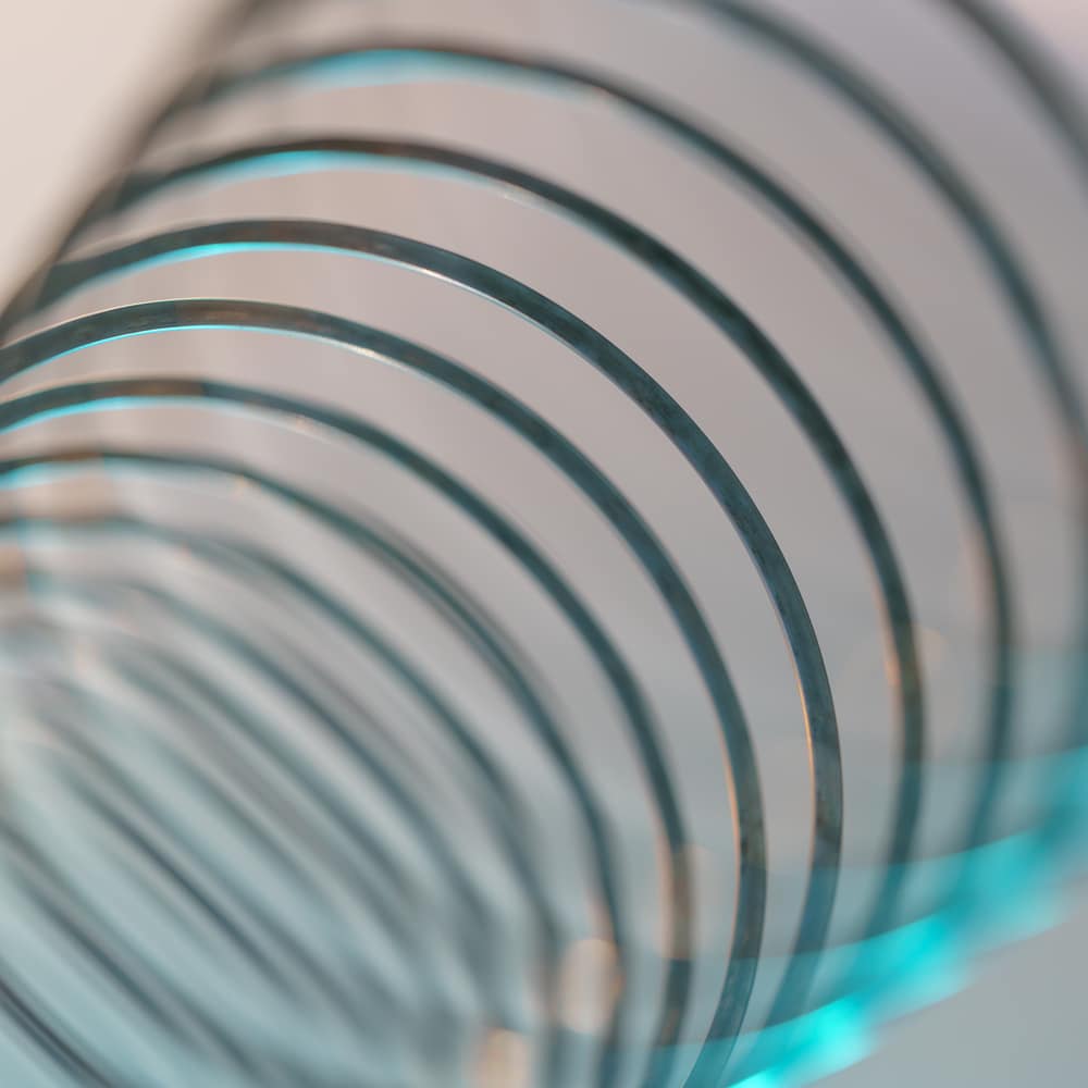 Closeup of coiled metal spring with sufficiently high strength and elastic properties in neon blue and yellow light. Macro photo, shallow depth of field.