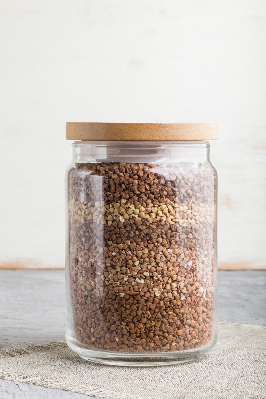 glass jar with buckwheat poured in layers on a gray and white background. side view, close up.