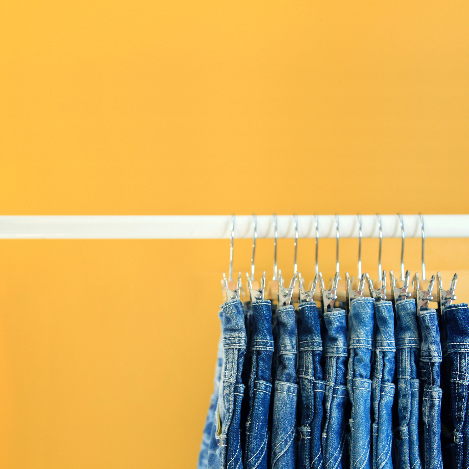 Row of hanged blue jeans with yellow background