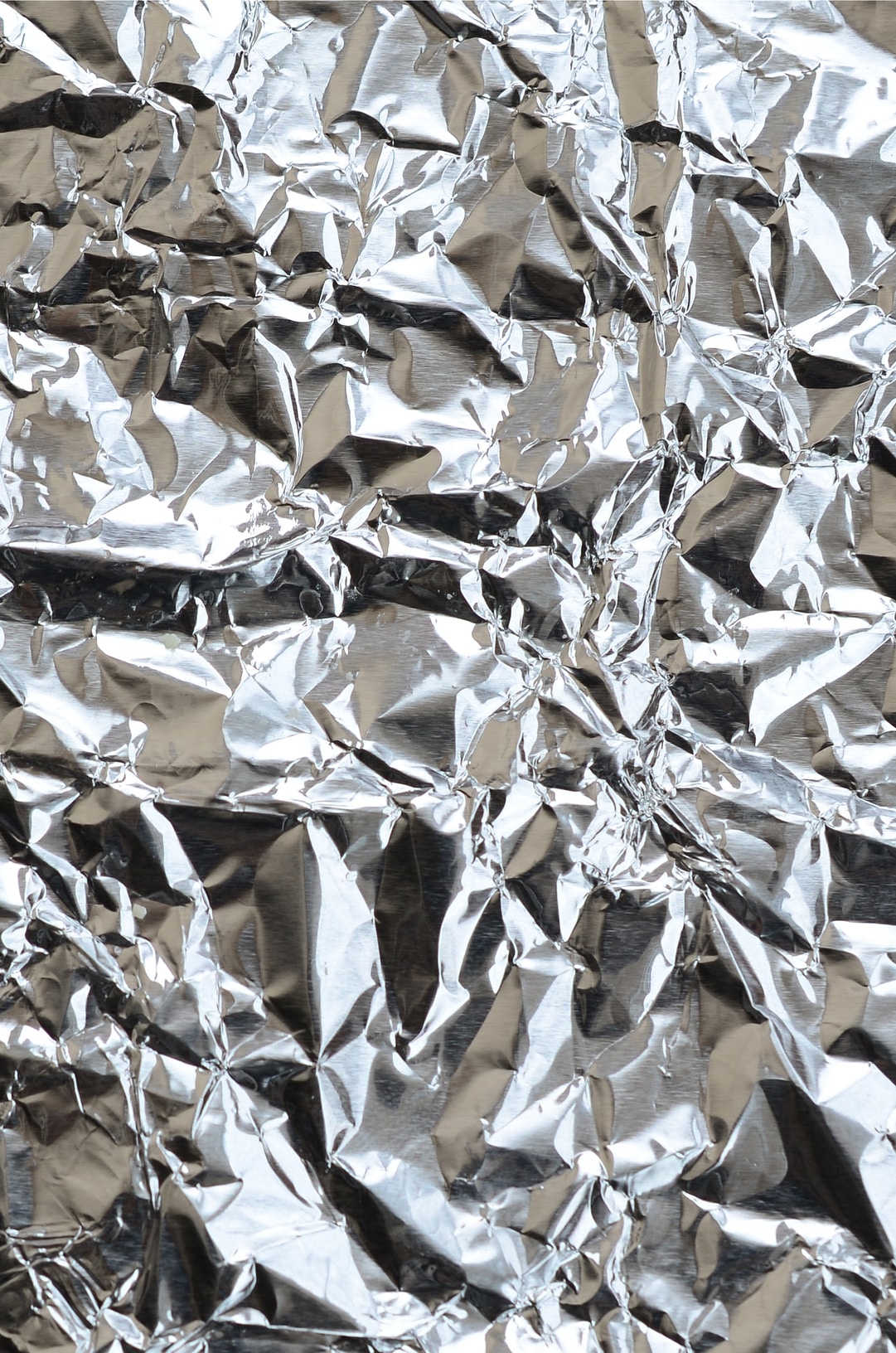 Thin wrinkled sheet of crushed tin aluminum silver foil background with shiny crumpled surface for texture