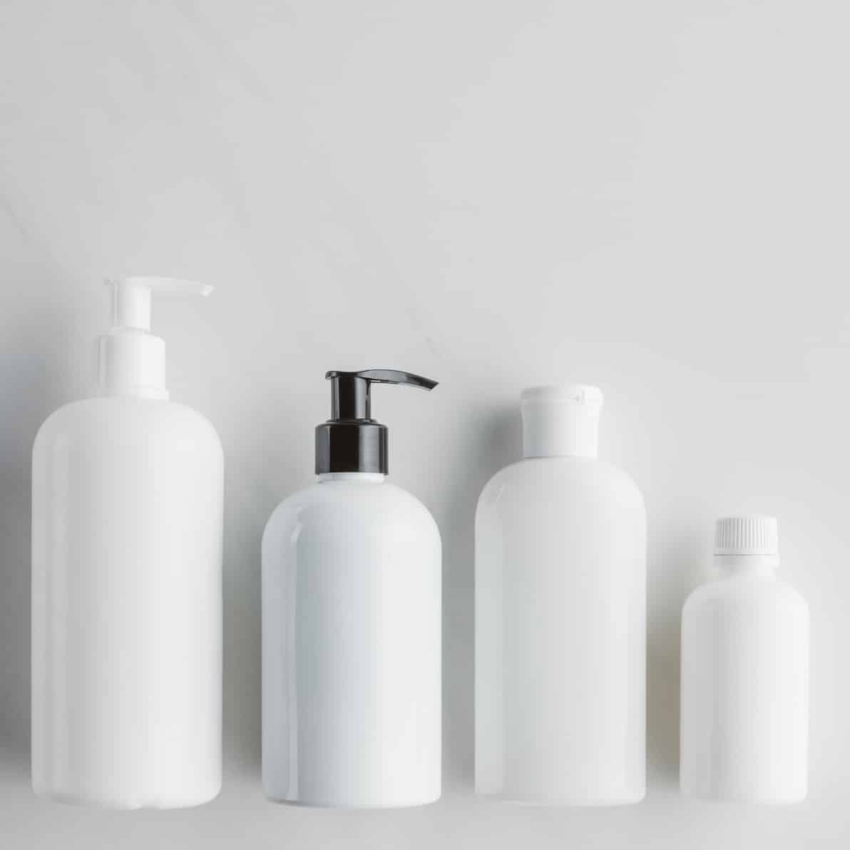top view of four white bottles of cream on white surface, beauty concept