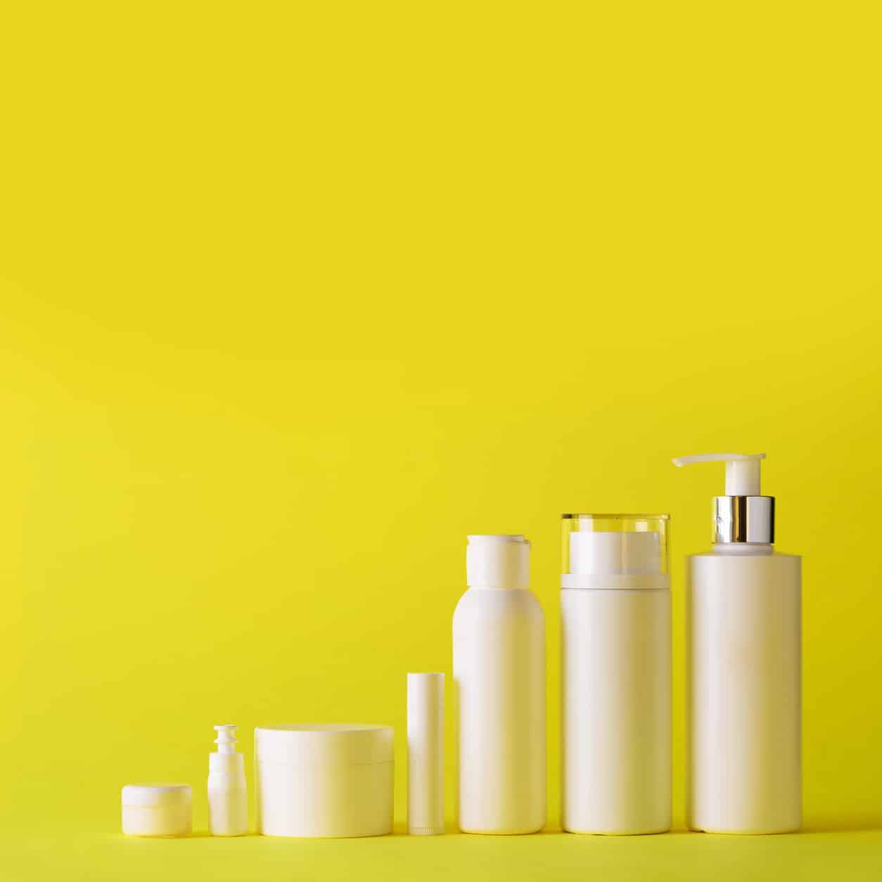 White cosmetic tubes on yellow background with copy space. Skin care, body treatment, beauty concept. Square crop.