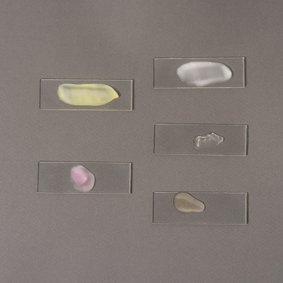 Multicolored smears of face cosmetics on laboratory glass on a gray background